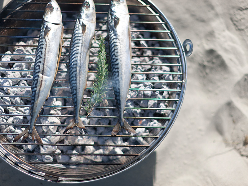Rock BBQ on a sandy beach grilling 3 silver fish